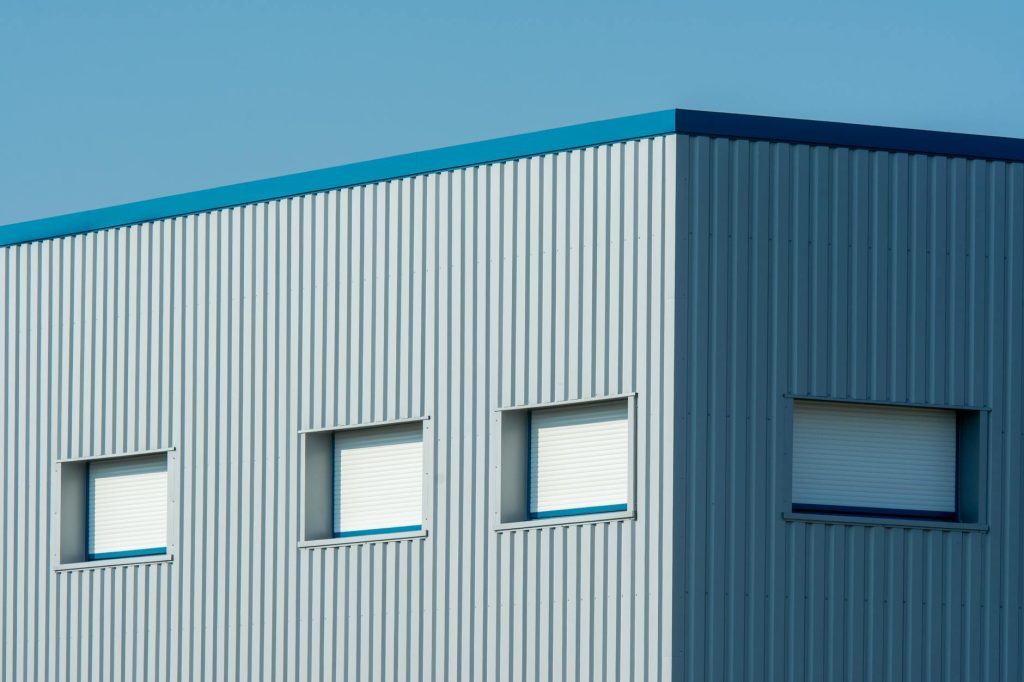 A sleek industrial building with a corrugated metal facade featuring roller blinds and sandwich panels.